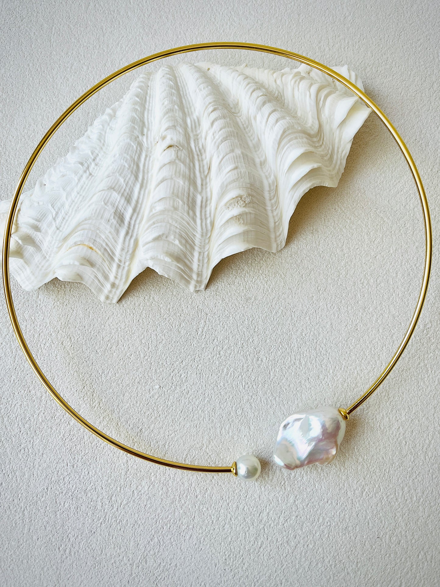 Gold necklace with a large white pearl pendant on a light gray background