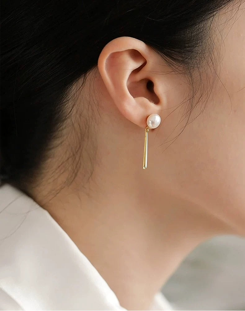 Gold earring with a pearl on an ear against a neutral background