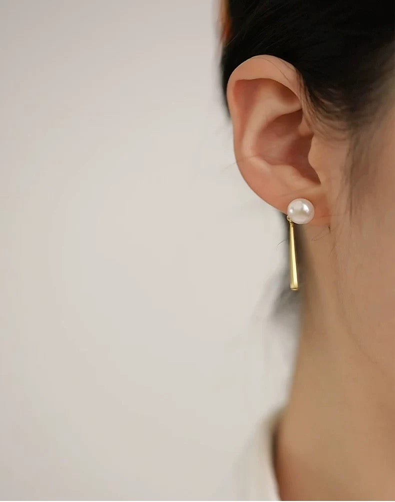 Pearl earring worn on a person's ear against a plain background