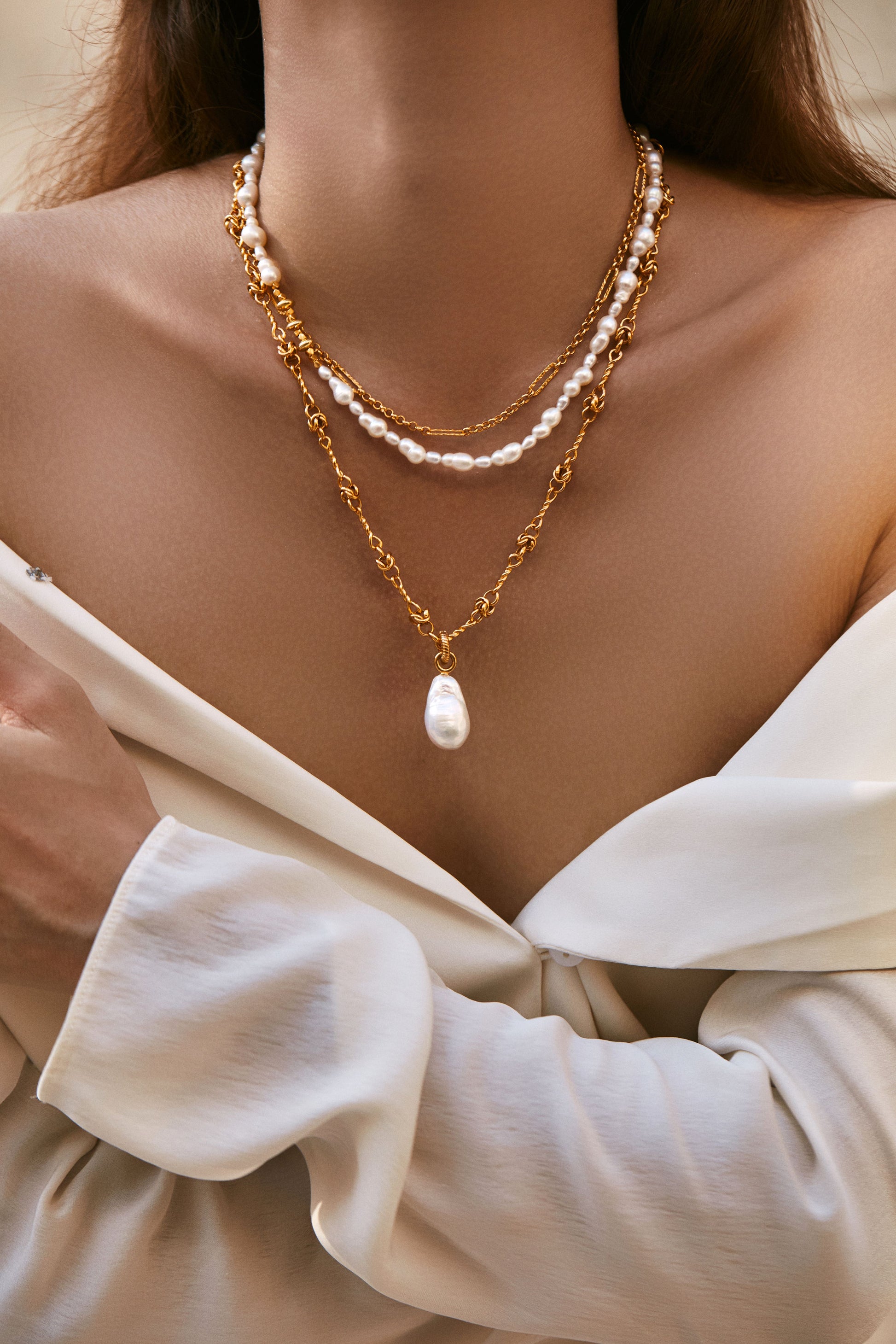 Close-up of a woman wearing a gold necklace with a pearl pendant and another pearl necklace with white twin pearls.
