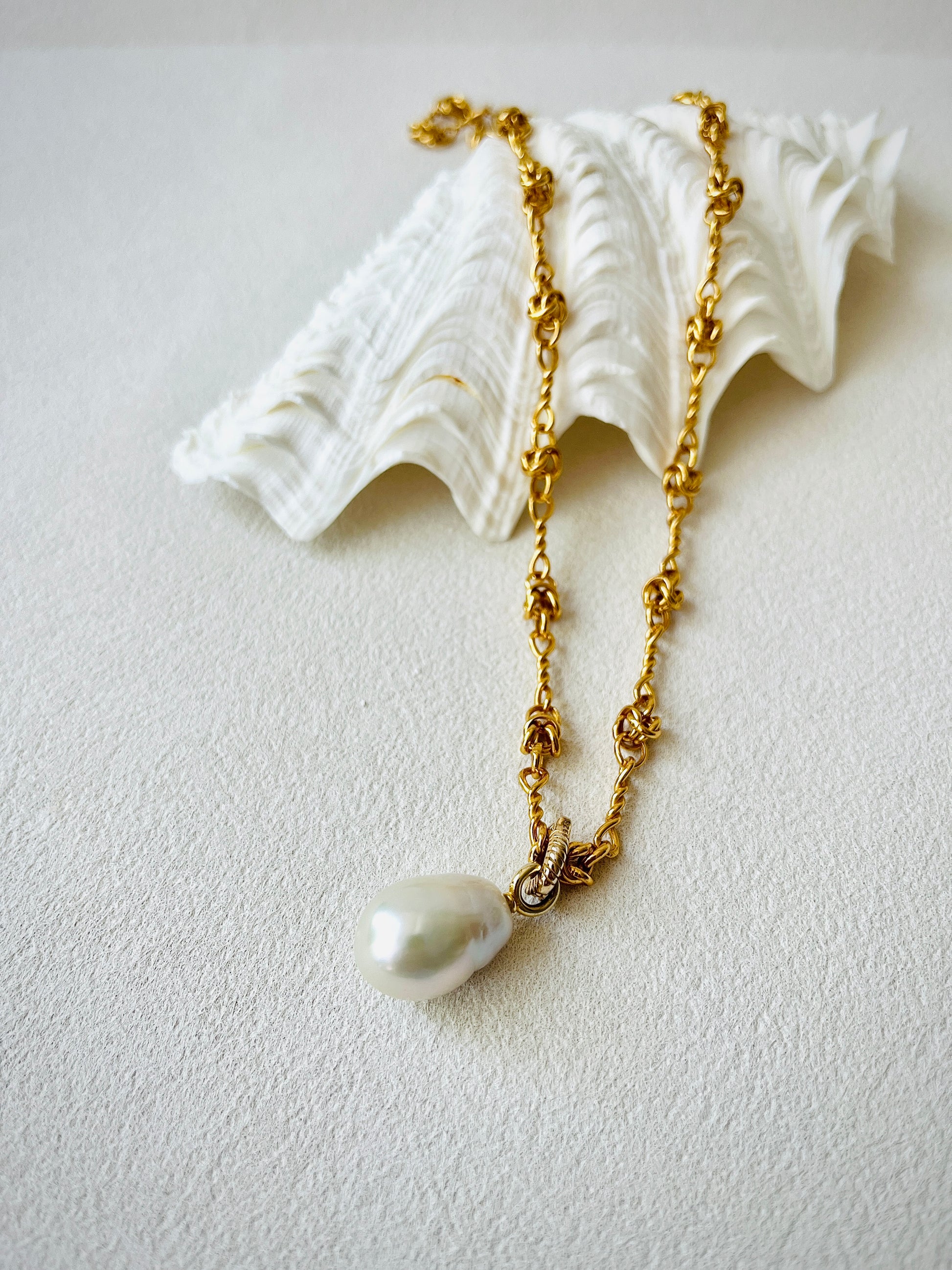 Gold chain necklace on a shell featuring a white freshwater pearl pendant