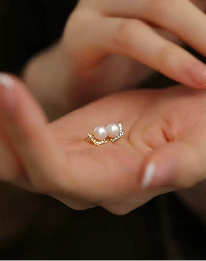 Close-up of a hand holding a ring with pearls and small diamonds.