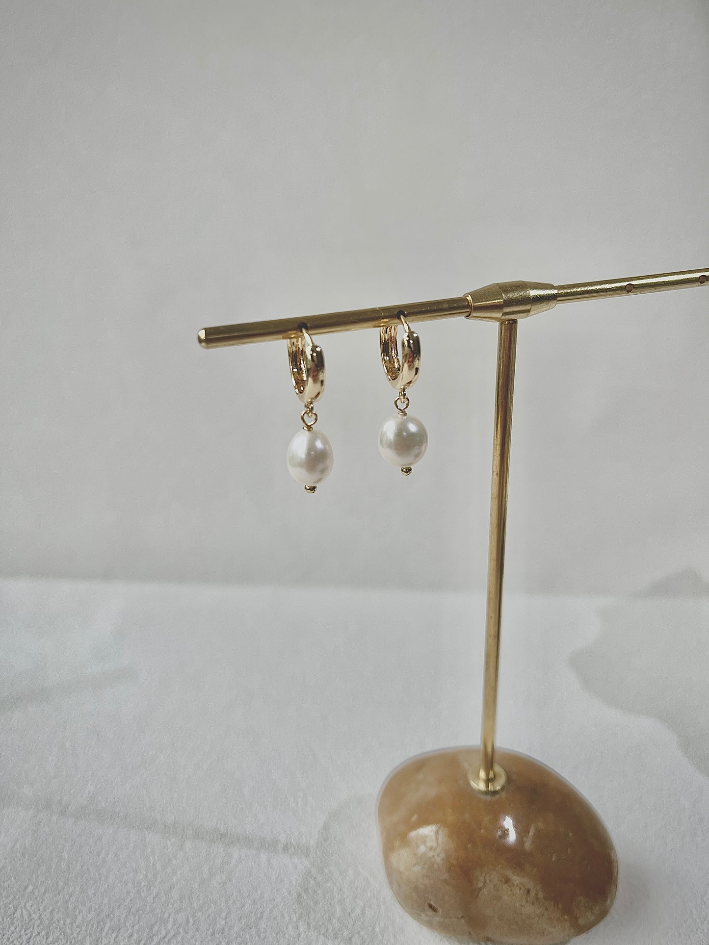 Pair of pearl earrings on a gold stand with a stone base against a light background