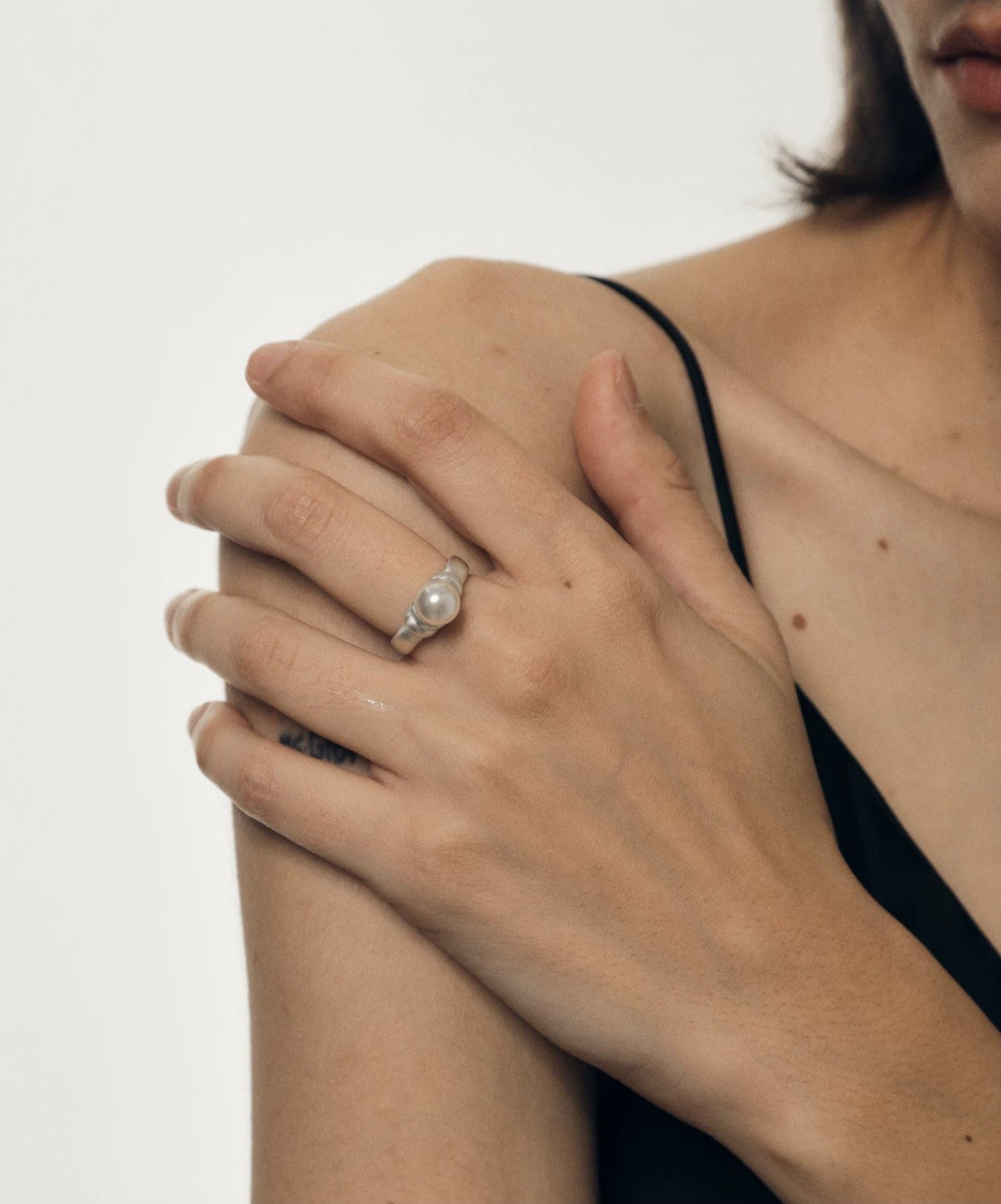 Close-up of a person wearing a pearl ring on a plain background