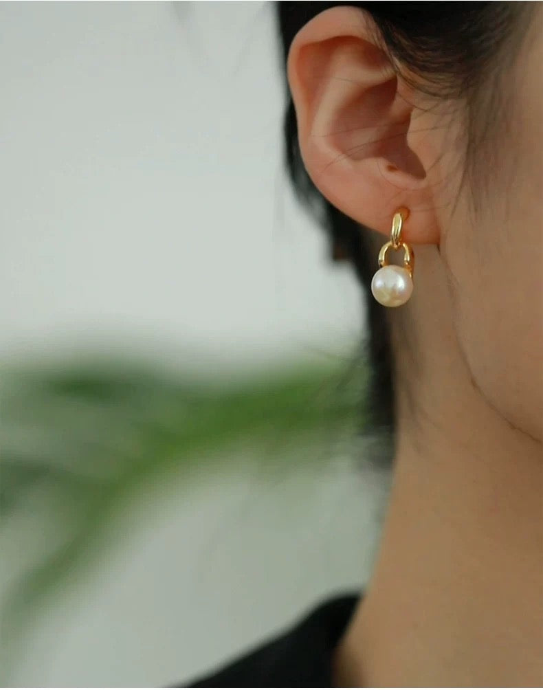 Gold earring with a pearl on an ear against a blurred background