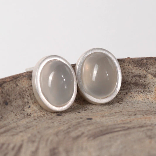 Silver earrings with a light stone-like center on a textured surface