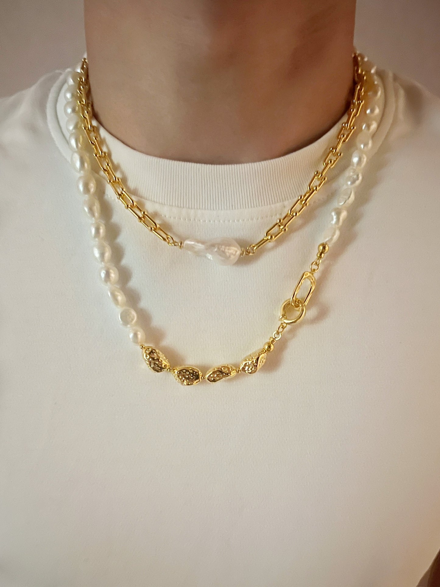 Gold chain and pearl necklace on a plain background