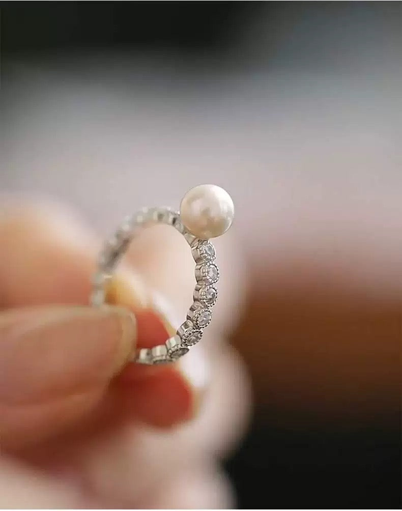 Close-up of a ring with a pearl and diamonds held between fingers against a blurred background