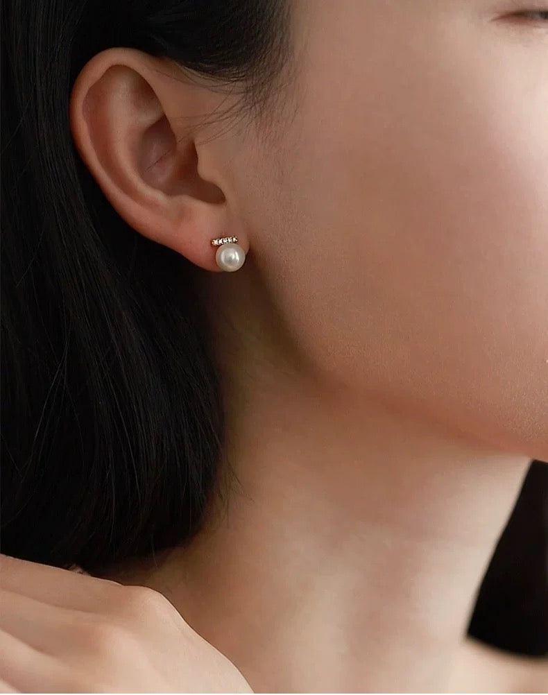 Close-up of a person wearing pearl stud earrings with a blurred background