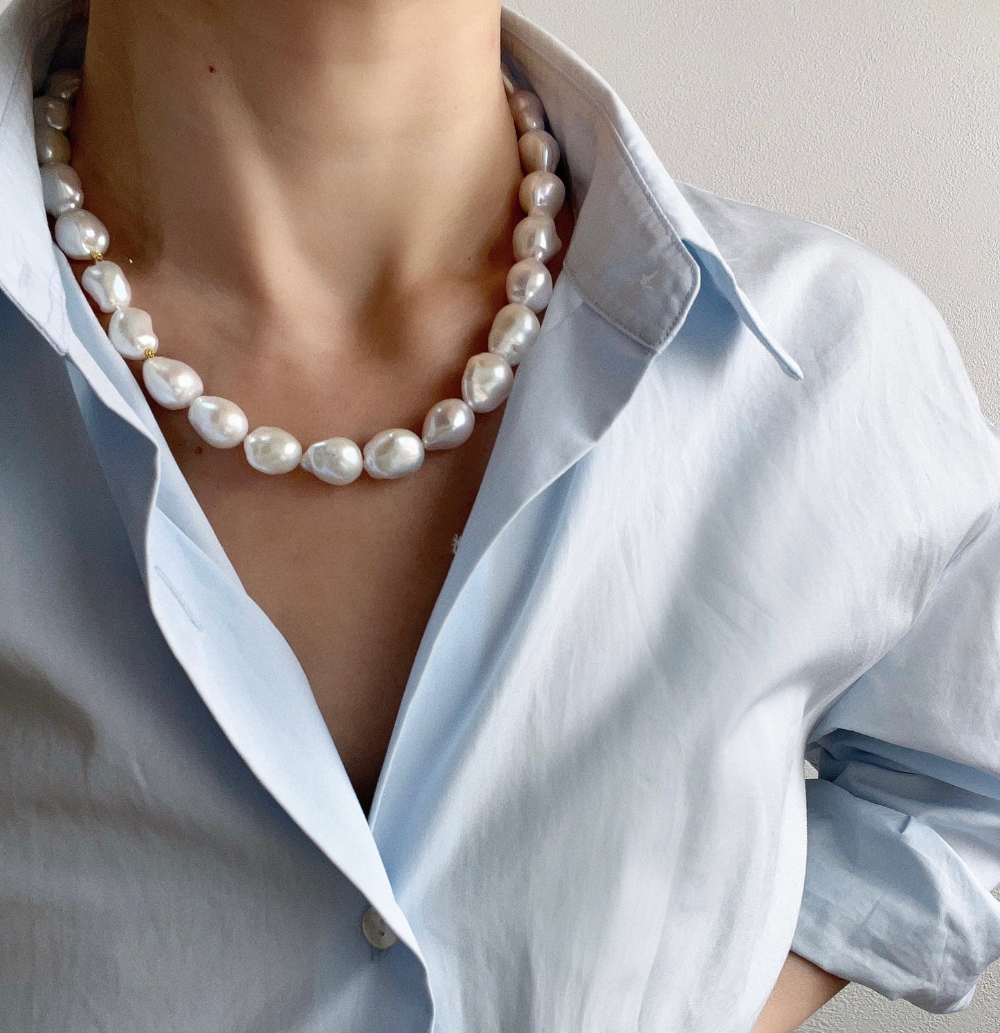 Person wearing a Baroque pearl necklace with a light blue shirt against a neutral background