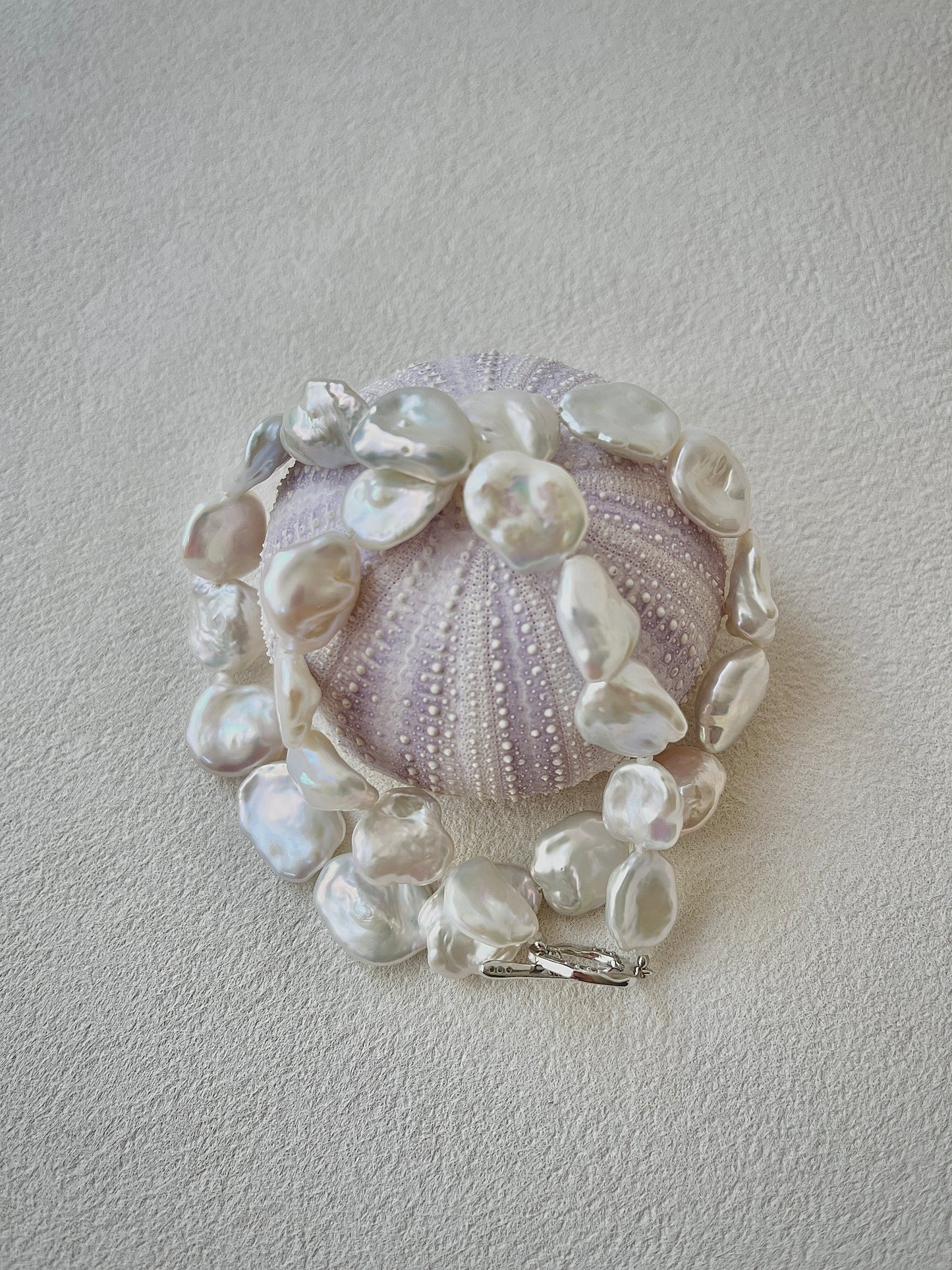 Bracelet with pearls and a central shell-like design on a light gray background