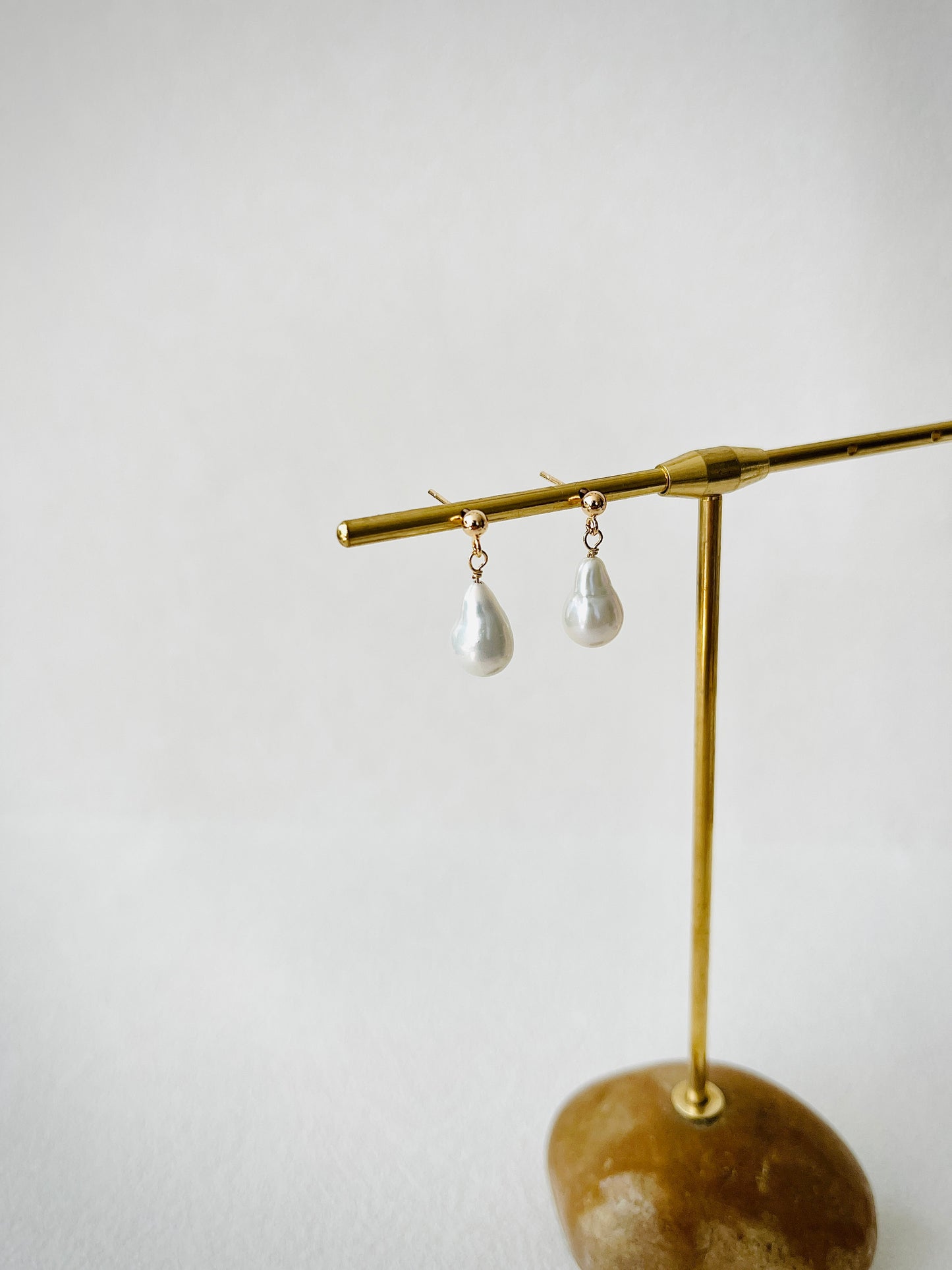 Pair of pearl earrings on a gold earring stand against a white background