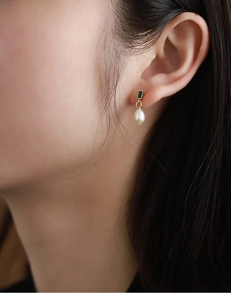 Close-up of an ear wearing a pearl earring with a dark gemstone.