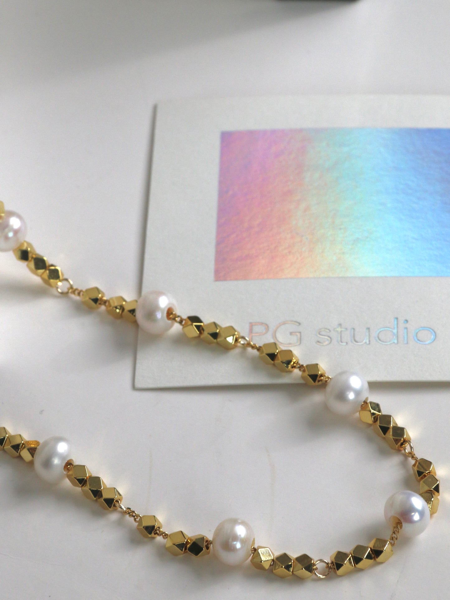Gold and pearl necklace for men on a white surface with a colorful card in the background