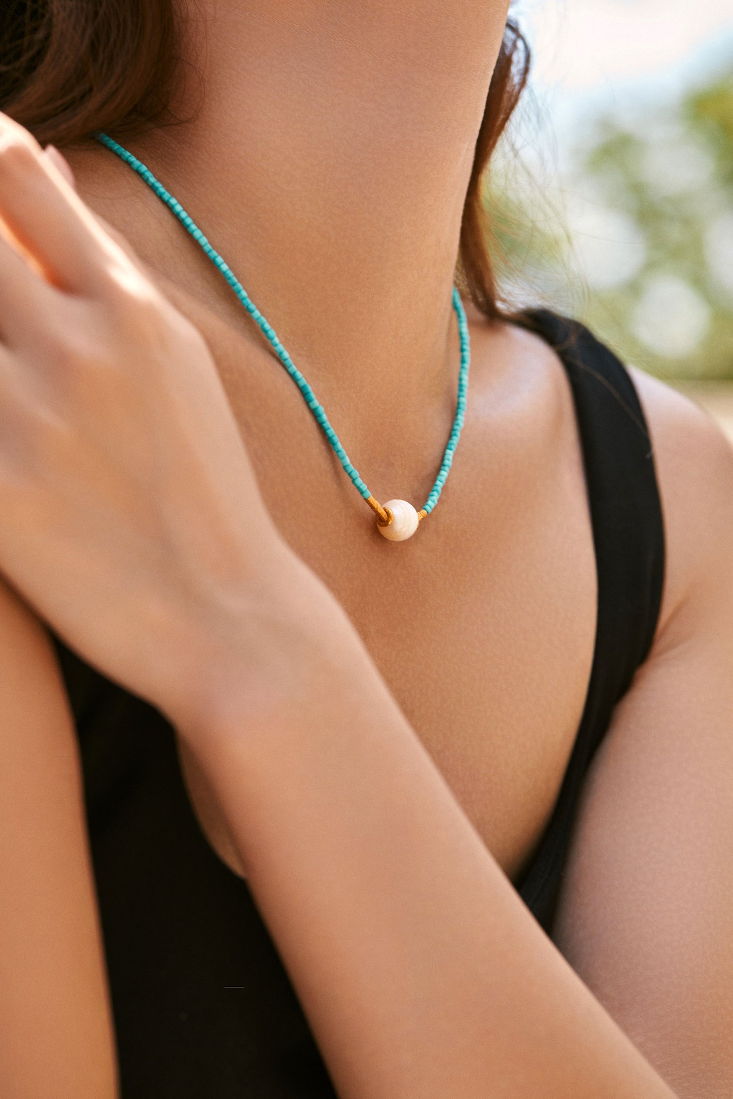 Close-up of a person wearing a turquoise beaded necklace with a pearl pendant.