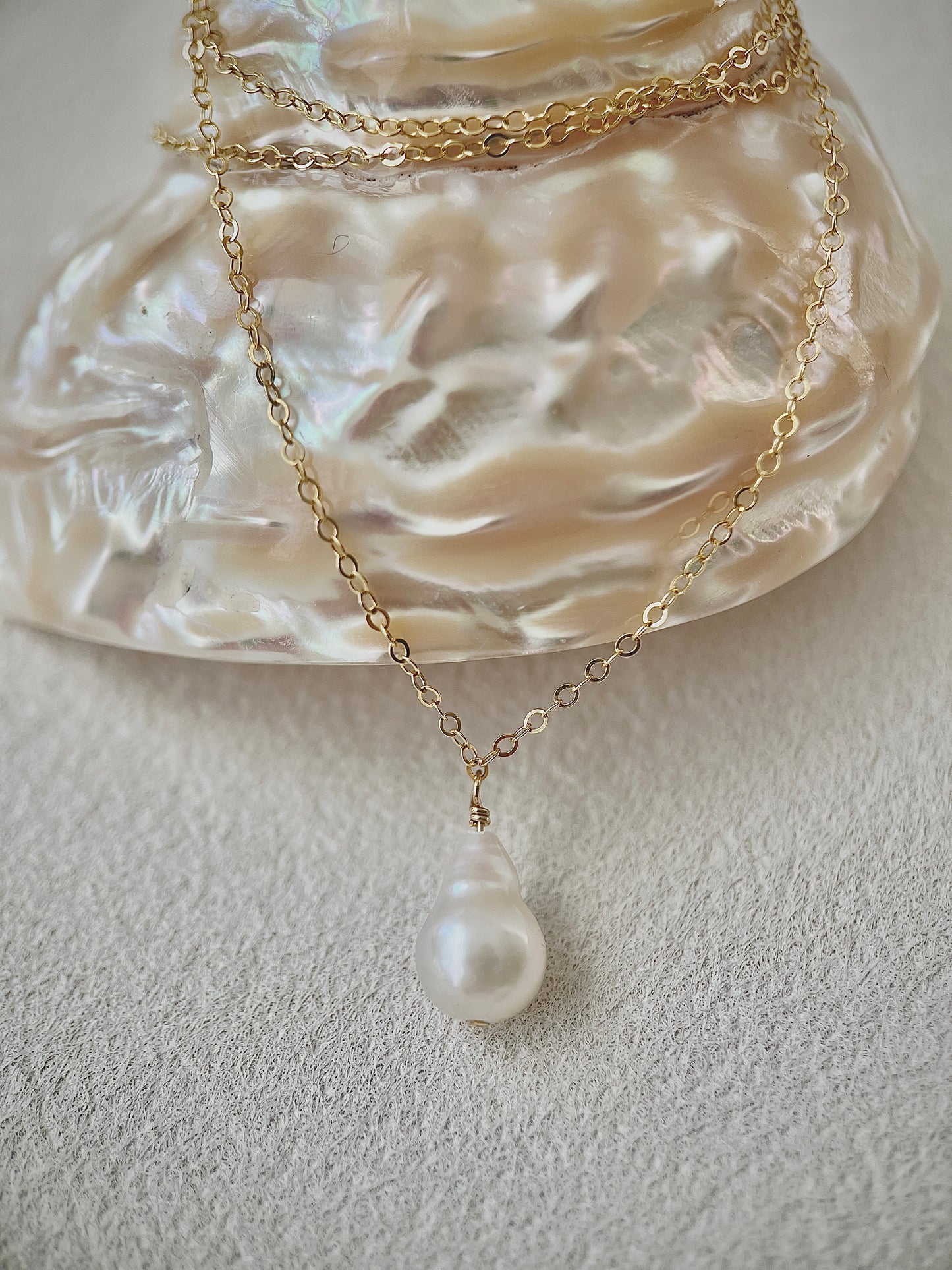 Gold necklace with a pearl pendant on a textured white surface
