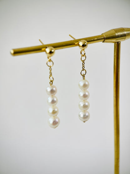 Pearl earrings on a gold stand against a white background