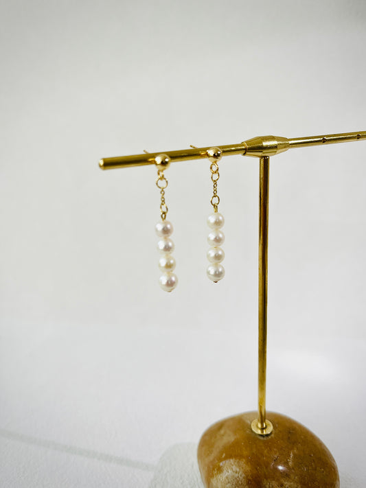 Pearl earrings on a gold stand against a white background