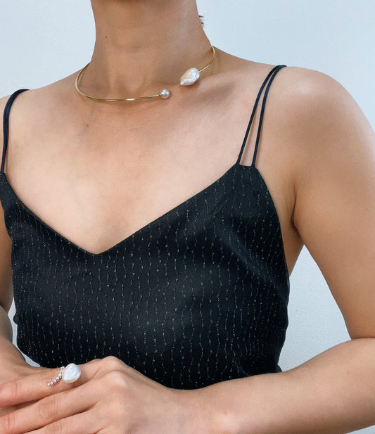Person wearing a black sleeveless top with thin straps and pearl jewelry on a light gray background