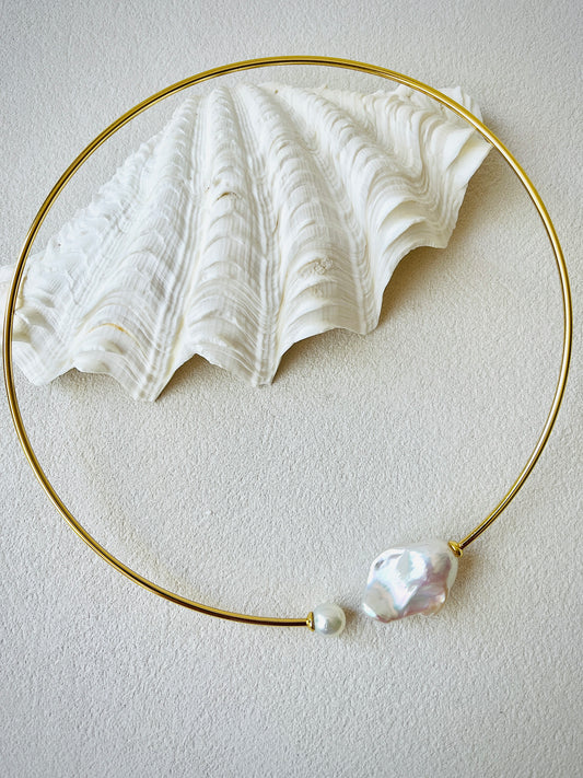 Gold necklace with a large white pearl pendant on a light gray background