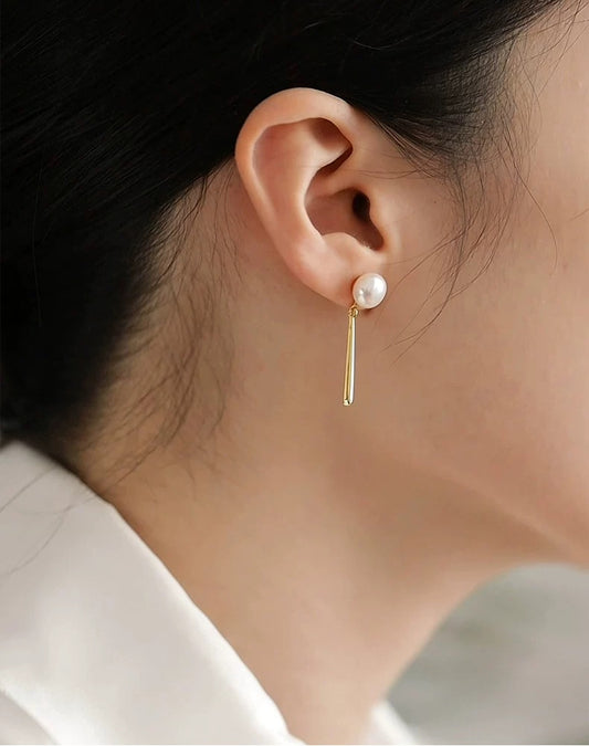 Gold earring with a pearl on an ear against a neutral background