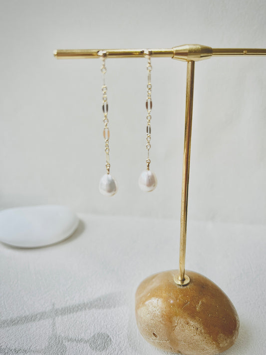Gold earrings with pearl drops on a decorative stand against a light background