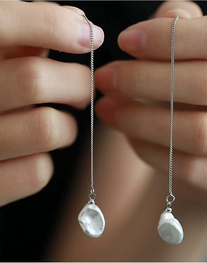 Silver earrings with pearl drops held between fingers against a blurred background