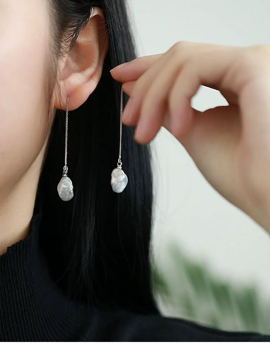 Person wearing pearl drop earrings with a blurred background