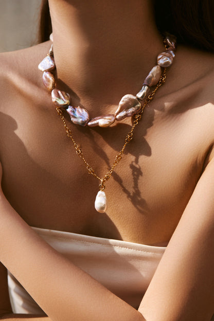 Close-up of a person wearing a chunky pearl necklace combined with a baroque pearl pendant on a gold necklace