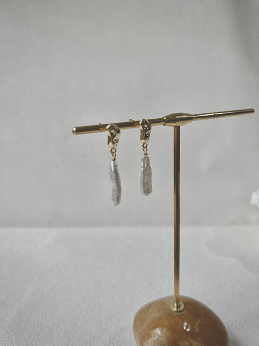 Pair of earrings on a gold stand against a light gray background