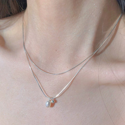 Close-up of a silver necklace with a pendant on a person's neck
