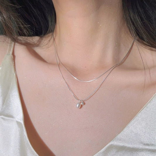 Close-up of a delicate necklace with a pendant on a person wearing a white top.