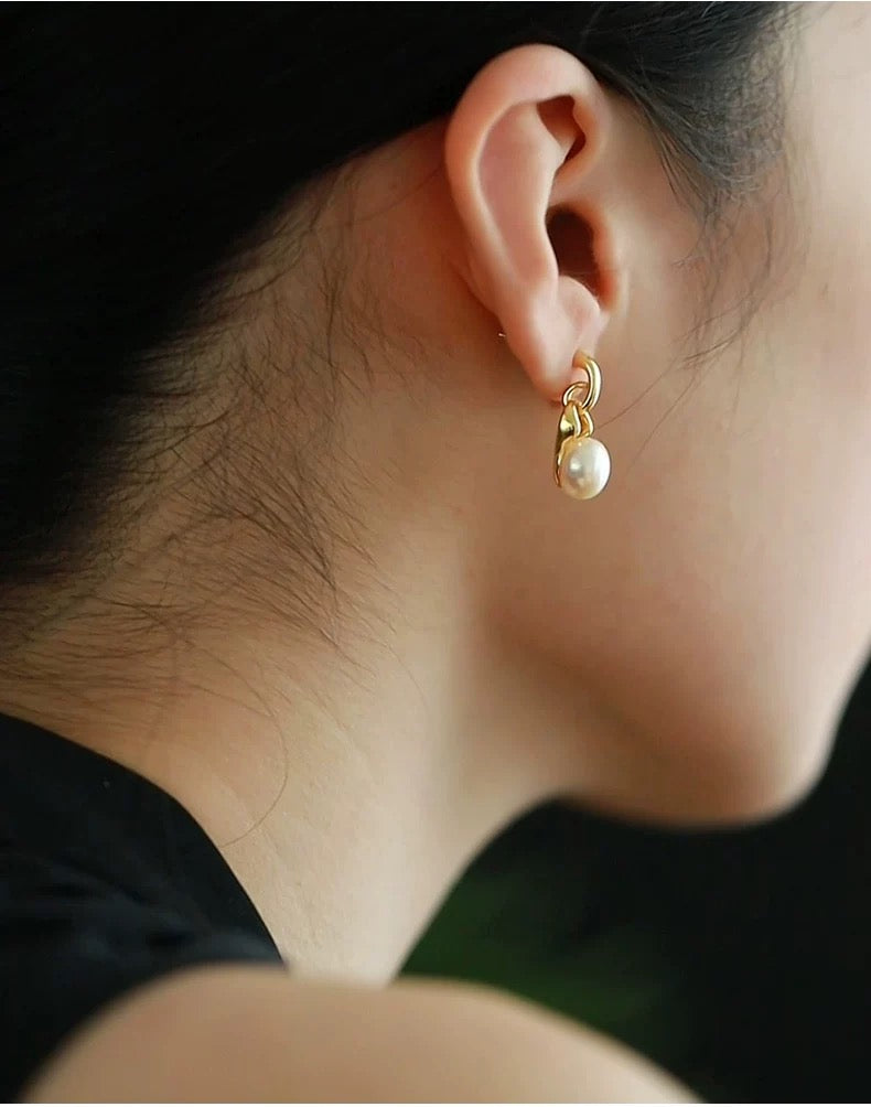 Close-up of an ear wearing a gold earring with a pearl drop.
