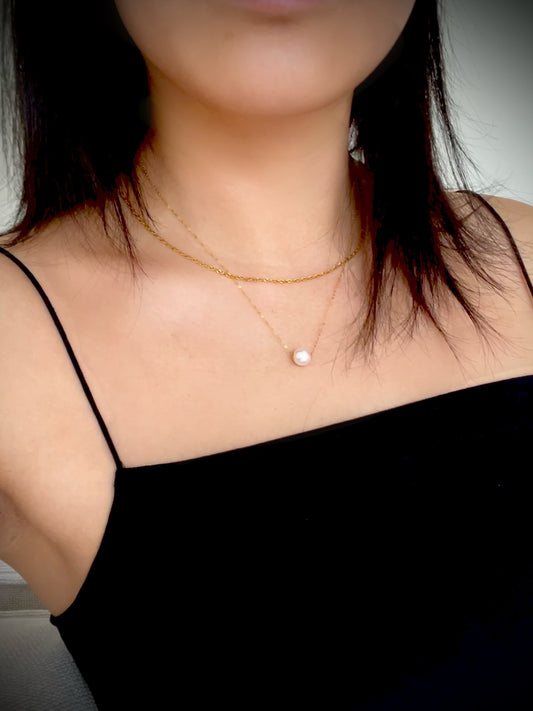 Person wearing a gold necklace with a pearl pendant against a neutral background