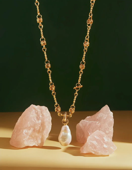 Gold necklace with a pearl pendant on a dark green background with pink stones.