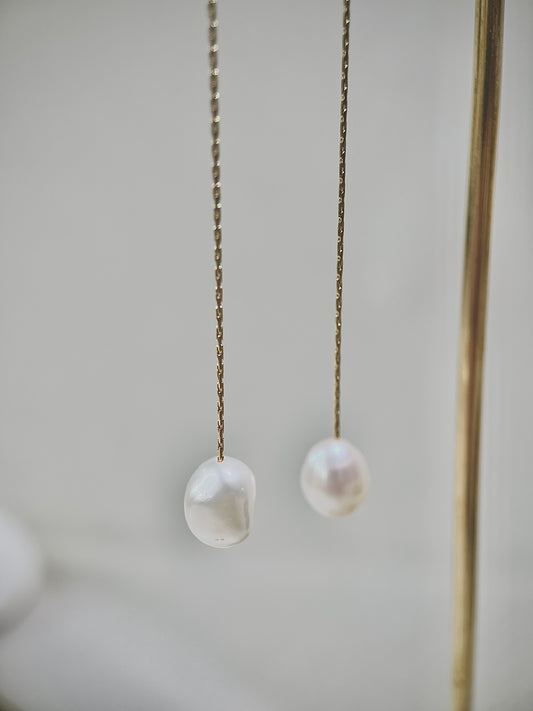 Two pearl earrings hanging on a chain against a neutral background