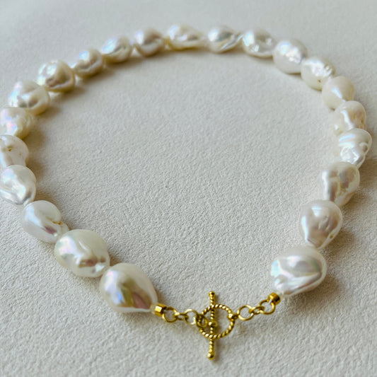 Baroque Pearl with a gold clasp on a light gray background