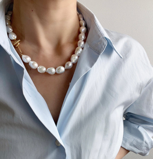 Pearl Pearl necklace worn by a person wearing a light blue shirt against a neutral background