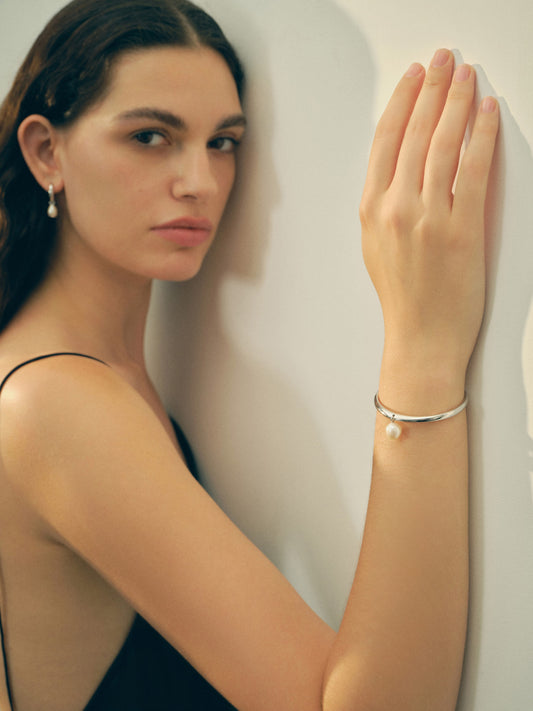 Woman wearing a pearl bracelet against a plain background