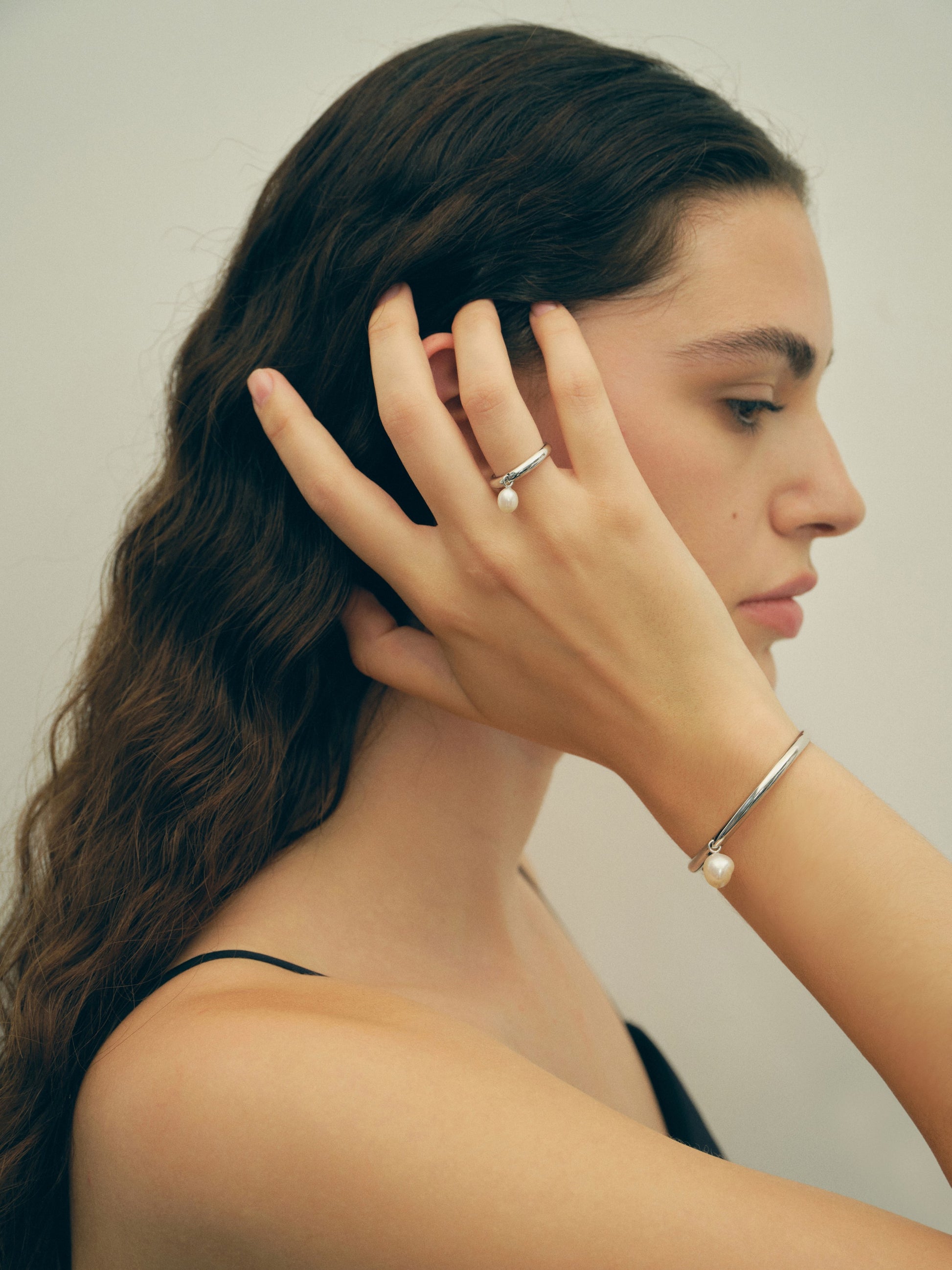 Woman wearing a pearl ring against a neutral background