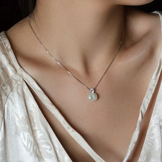 Necklace with a pearl pendant worn by a person in a light-colored top.