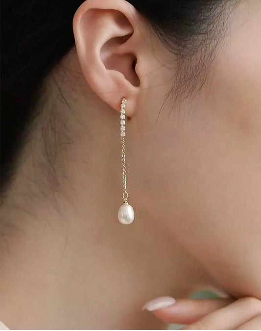 Pearl earring worn by a person, close-up of ear with dark background