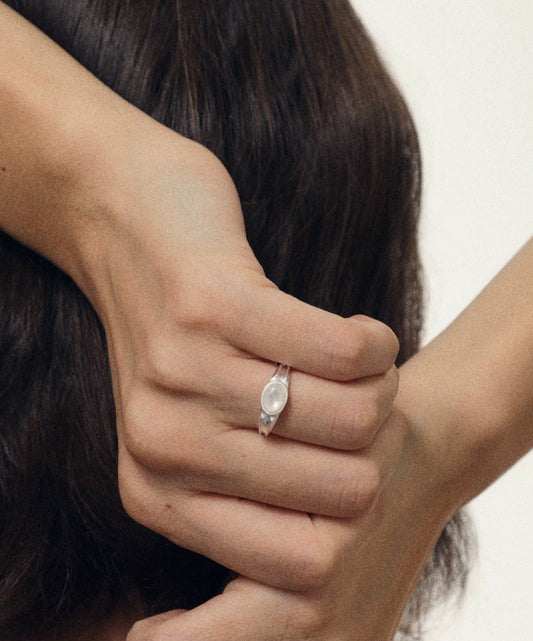 Close-up of a hand wearing a silver ring with a nacre on a neutral background