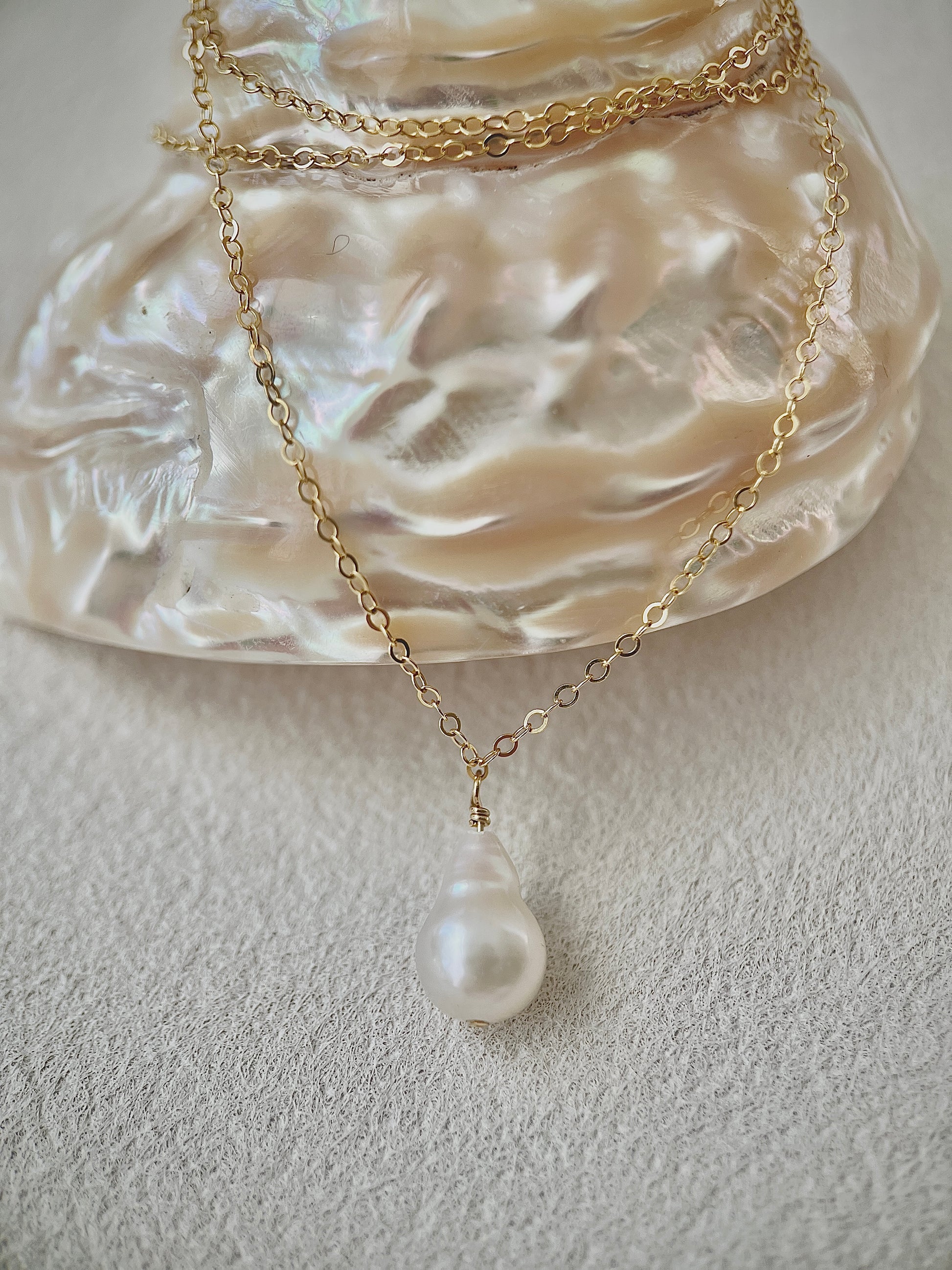 Gold necklace with a pearl pendant on a textured white surface