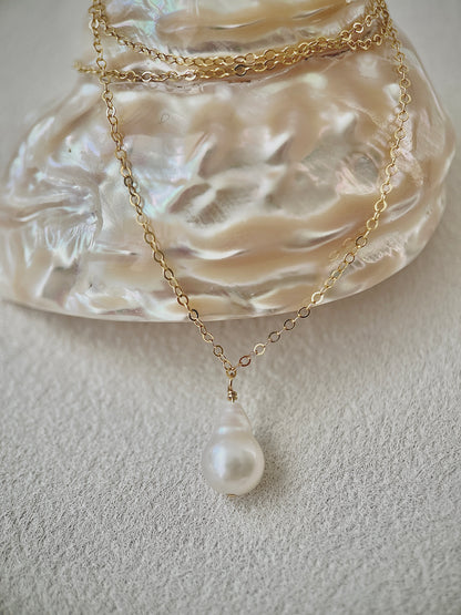 Gold necklace with a pearl pendant on a textured white surface